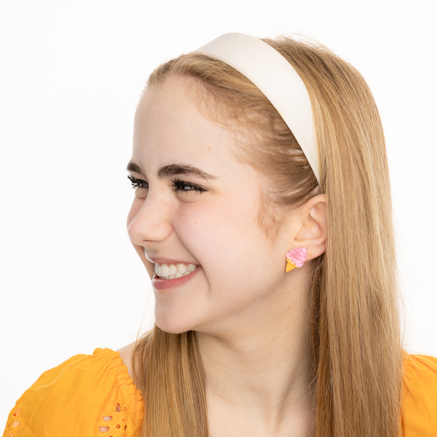 Teen girl with blonde, long, straight hair, wearing a white headband, looking to the side and smiling. She is wearing an orange top. She is also wearing the "Inspiring Ice Cream Earrings".
