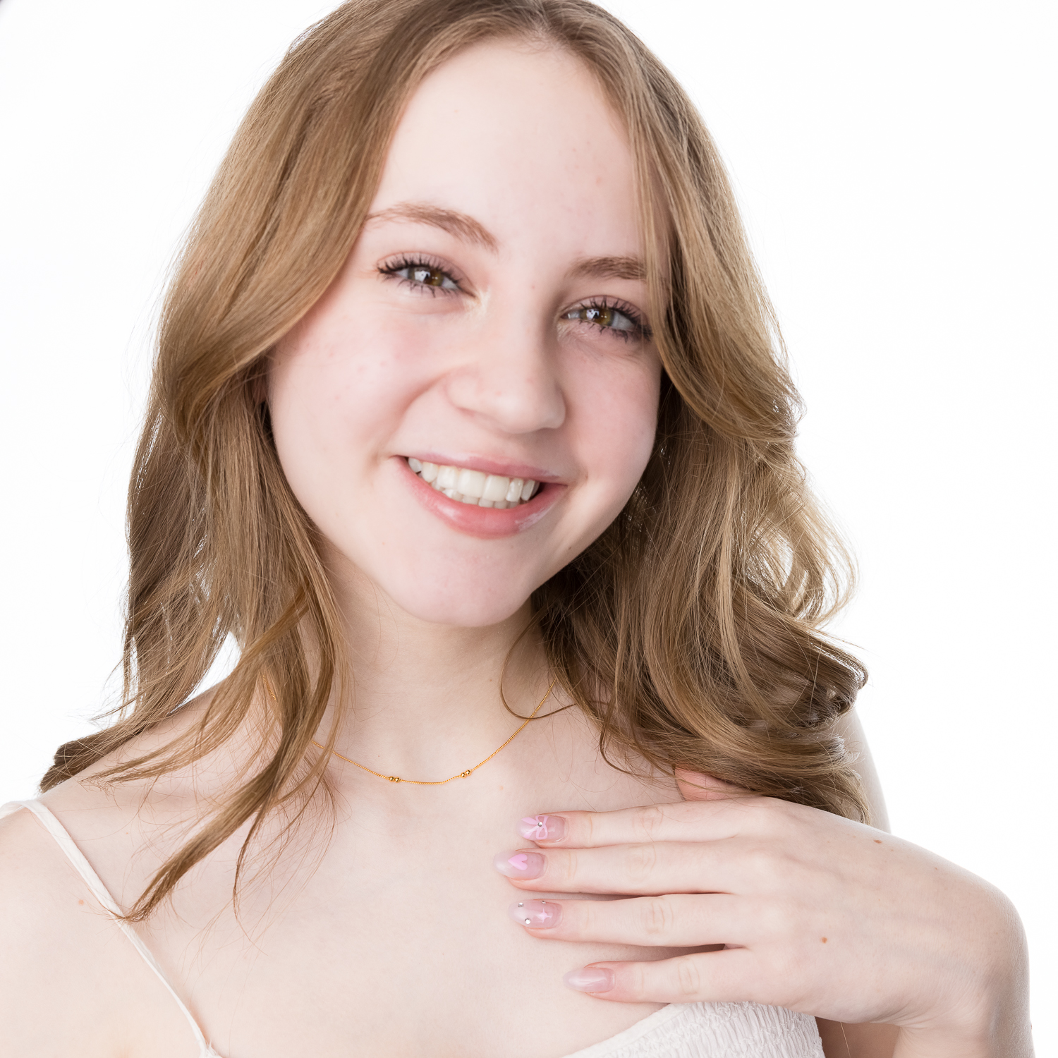 Teen girl with blonde, mid-length, curled hair, wearing a white top, the "Glow In Morse Code Necklace". She is smiling and touching the necklace.
