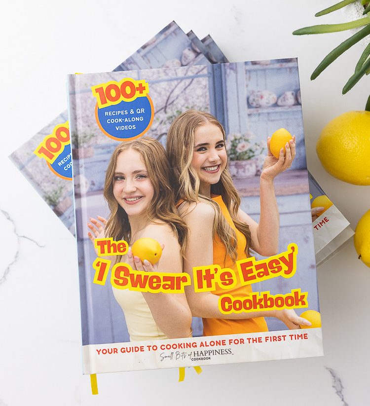 The 'I Swear It's Easy' Cookbook pile, on top of a white counter with a green plant and lemons.